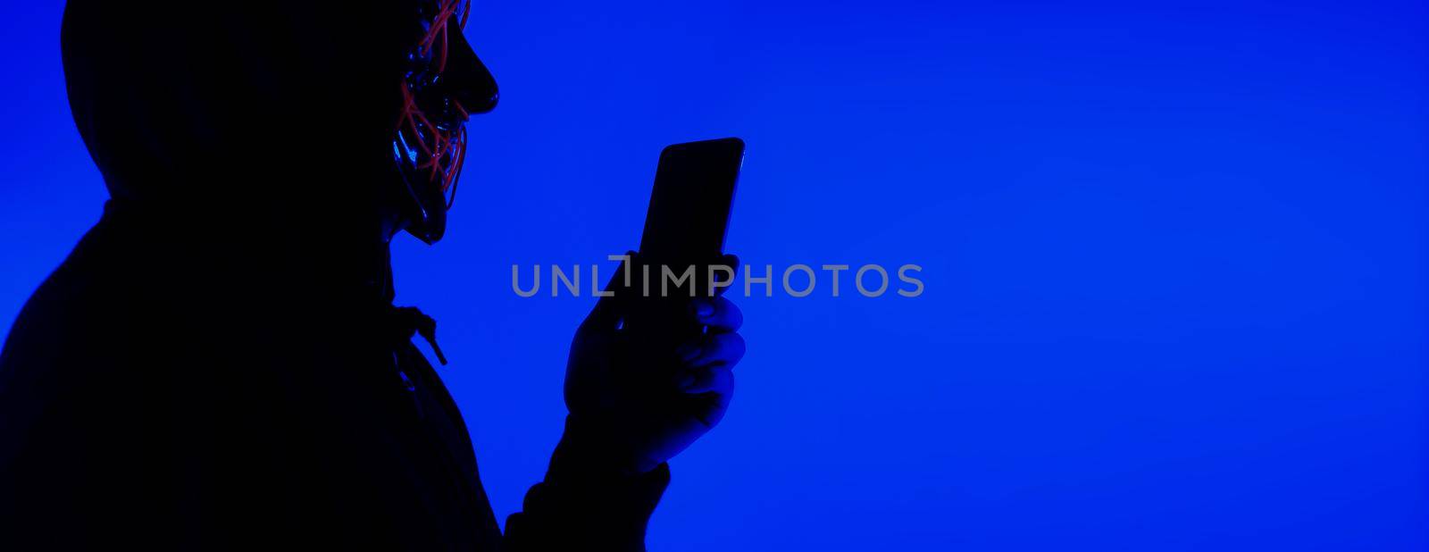 Digital security Concept. Anonymous hacker with mask holding smartphone hacked. by gnepphoto