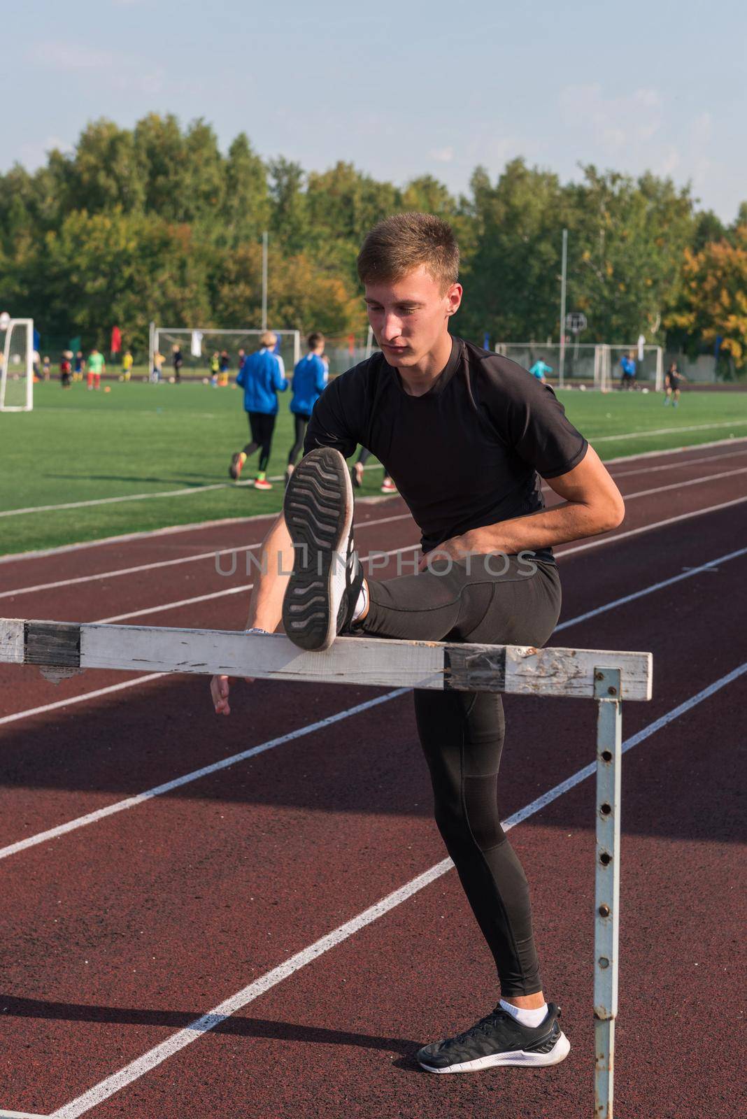 Young sporty man athlete runner in sportswear stretching before running hurdles on stadium