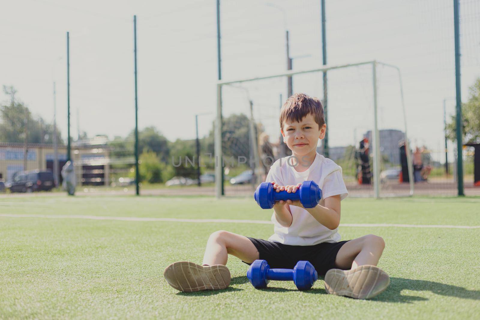 A child with dumbbells on the playground. A sporty kid. Illustrating an article about sports. Children's exercises. Education of champions. Light weightlifting. Lifestyle