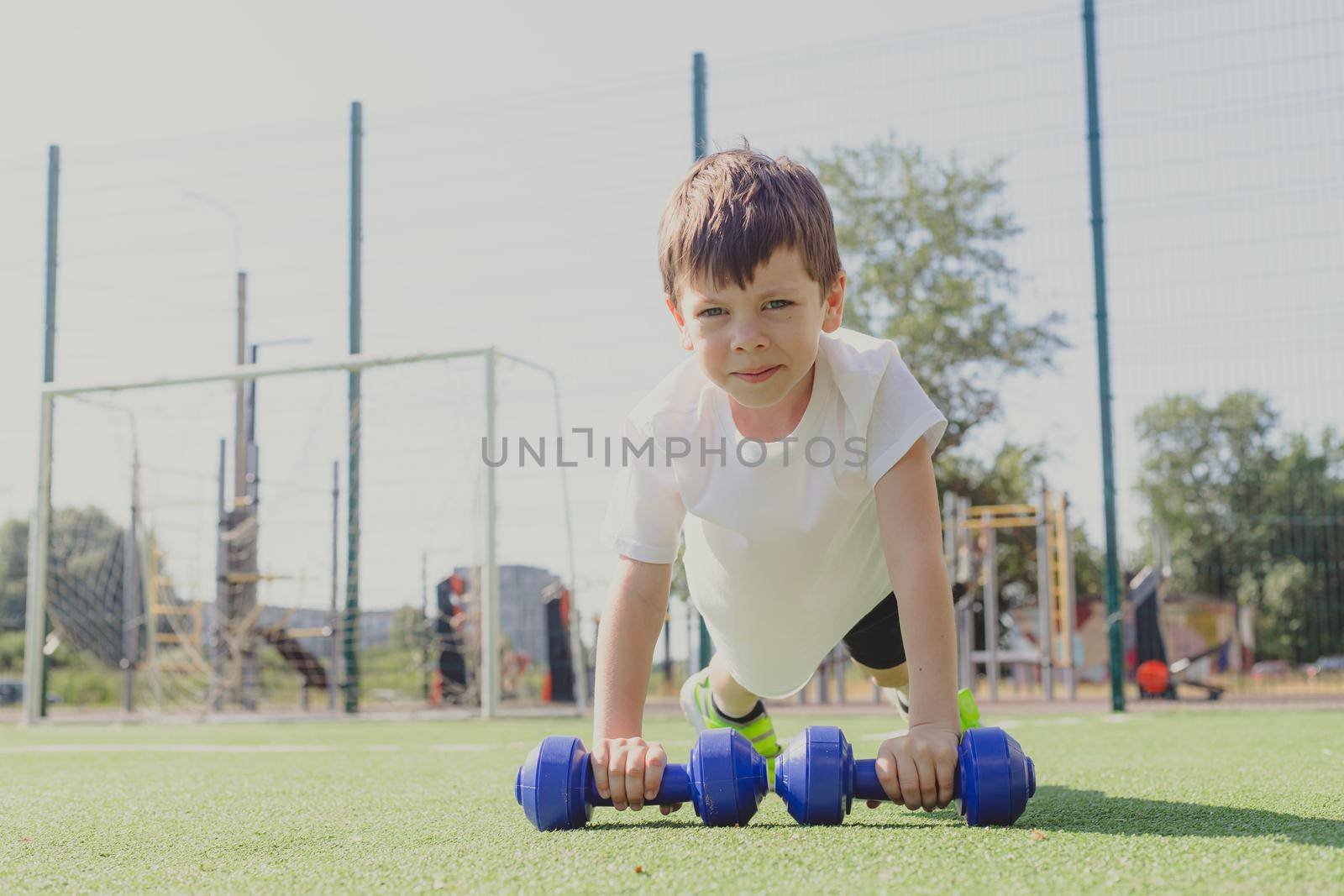 A child with dumbbells on the playground. A sporty kid. Illustrating an article about sports. Children's exercises. Education of champions. Light weightlifting. Lifestyle