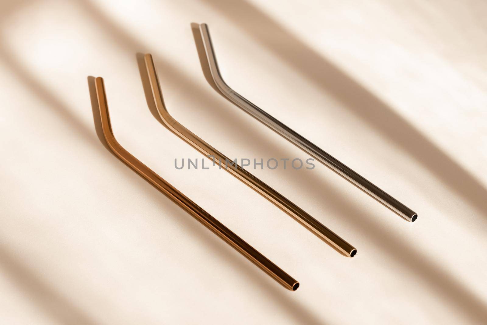 Reusable zero waste metal straw, eco friendly drinking straws from aluminium or stainless steel on neutral beige background with shadow from room windows, high angle view. Sustainability concept