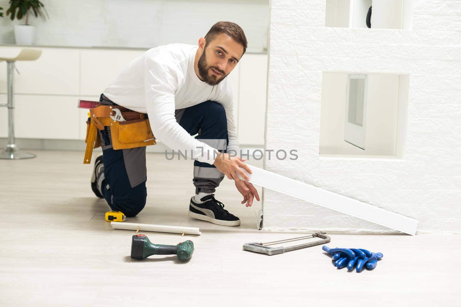 A man installs a floor skirting board. Fixing the plastic skirting board with screws to the wall. Home renovation