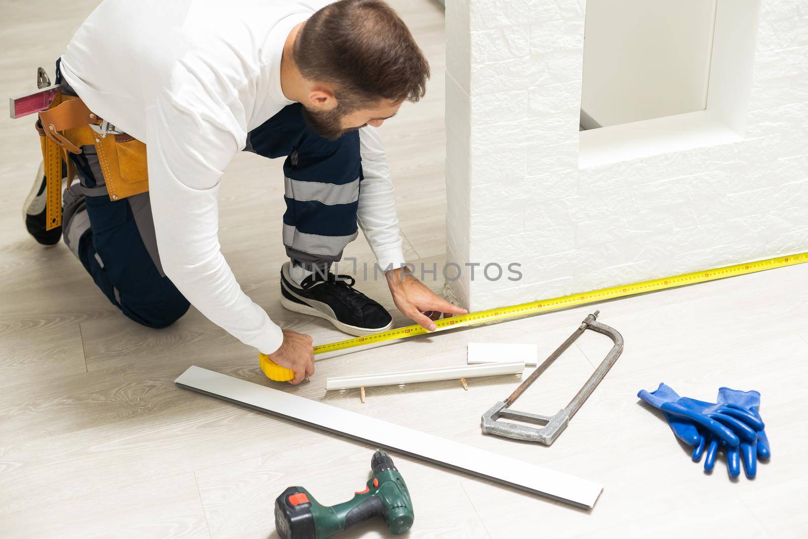 A man installs a floor skirting board. Fixing the plastic skirting board with screws to the wall. Home renovation