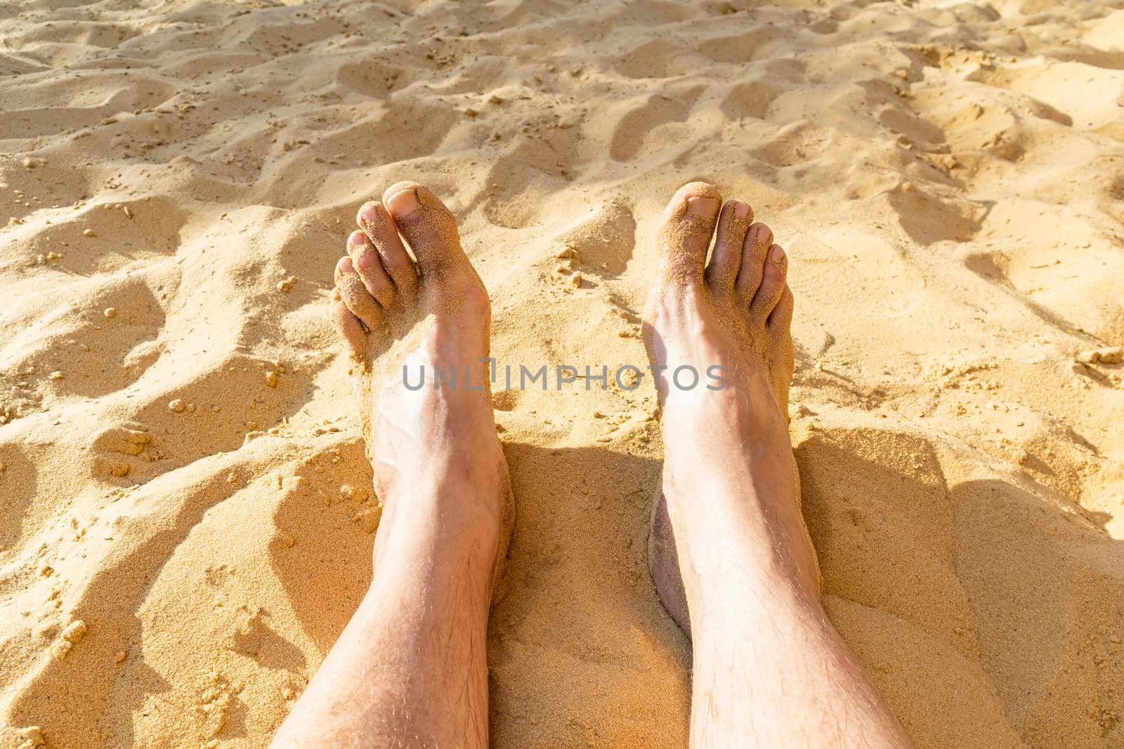 legs of a resting man on the sand close-up by roman112007