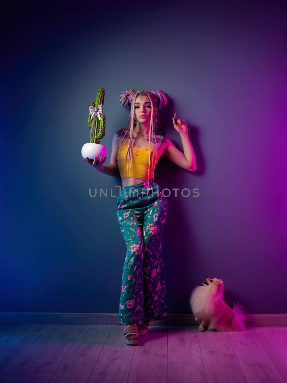 stylish girl with dreadlocks in fashionable bright clothes on a neon background with a small pomeranian dog by Rotozey