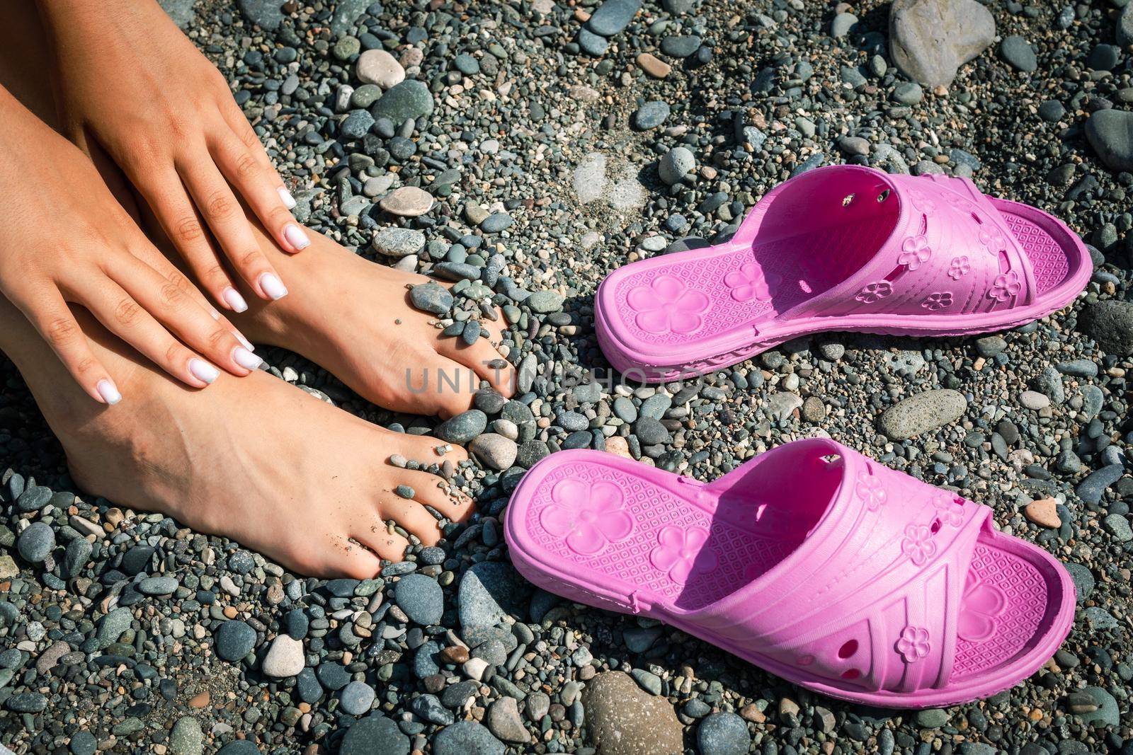 Women's hands and feet and rubber slippers on the background of stones on the beach.