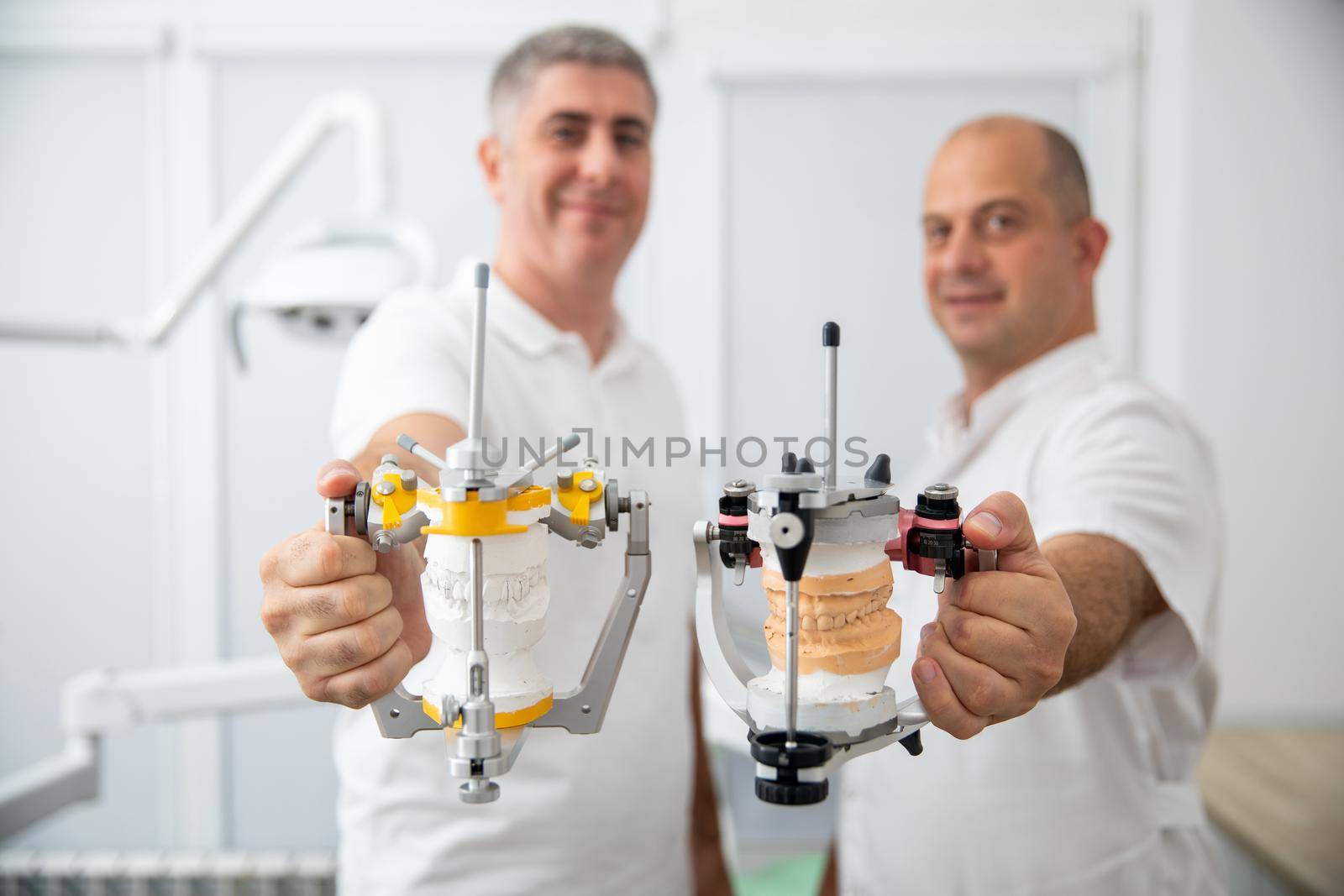 Two male dentists holding dental articulators in dental clinic by Mariakray