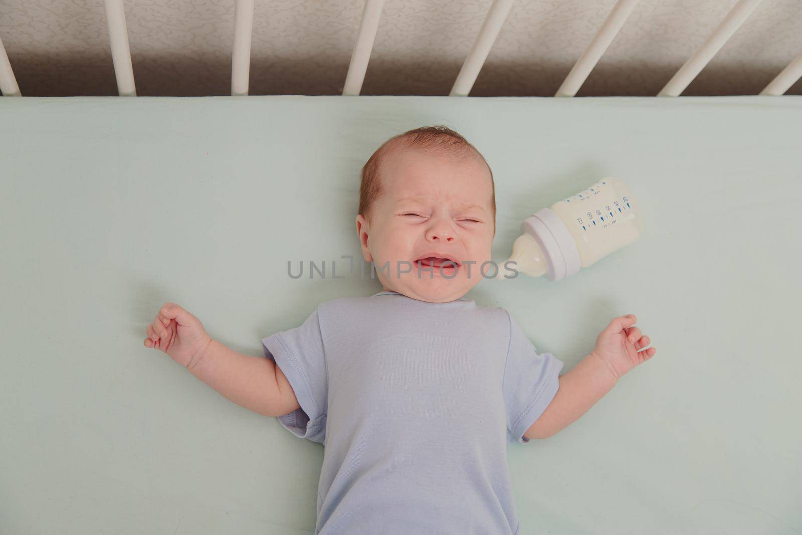 A hungry baby is crying in the crib . Baby crying. Children 's emotions . Pain during teething. A hungry child. Children's colic in the stomach. by alenka2194