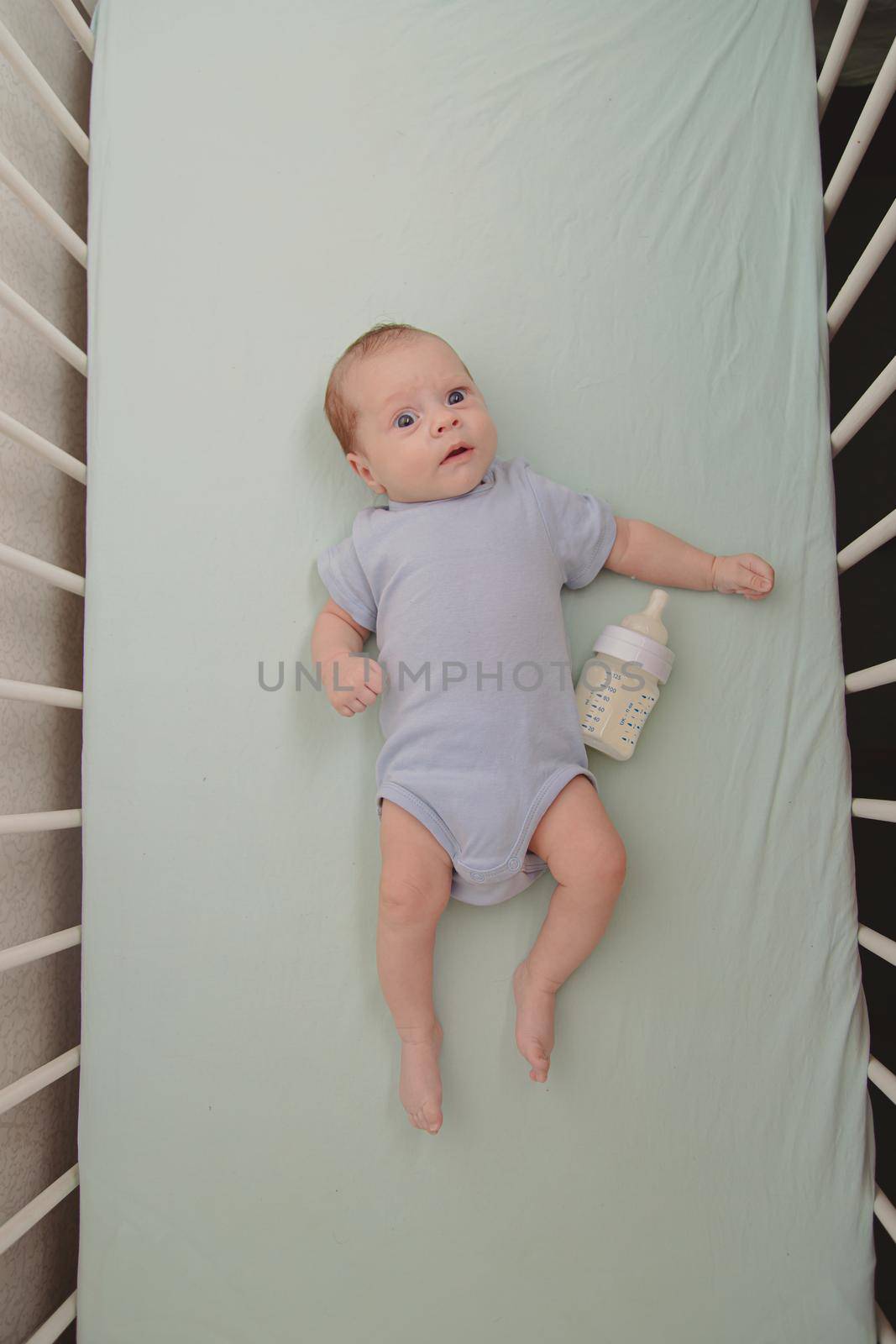 Baby with a bottle in the crib top view . Baby food copyspace . Children's food. Hungry baby. by alenka2194