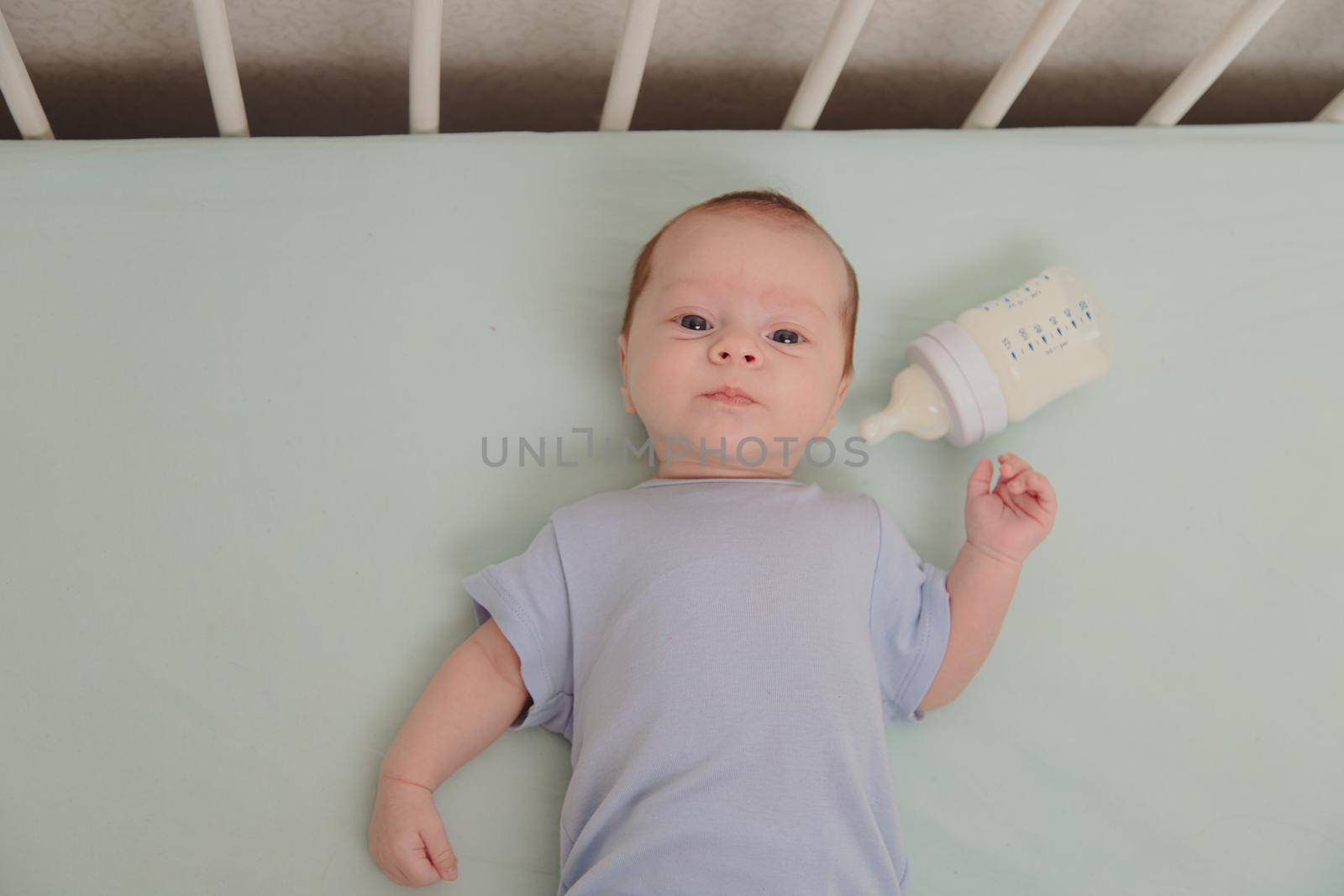 Baby with a bottle in the crib top view . Baby food copyspace . Children's food. Hungry baby. Infant formula .
