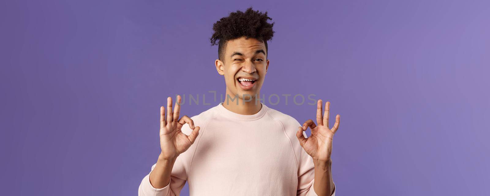 Close-up portrait of young confident and carefree man telling to relax and no problem, have all under control, wink assuring and show okay signs, guarantee best quality, good delivery service.