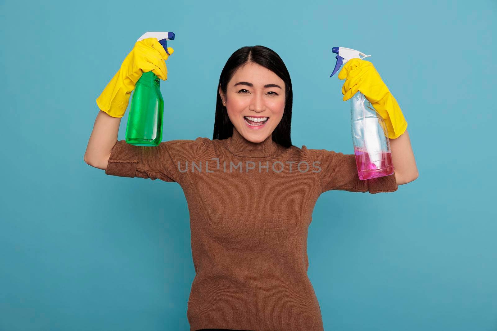Delighted glad asian housemaid raising arms holding two detergent sprays in the yellow gloves, Housewife worker, Cleaning home concept, Smiling cheerful and positive from day to day work