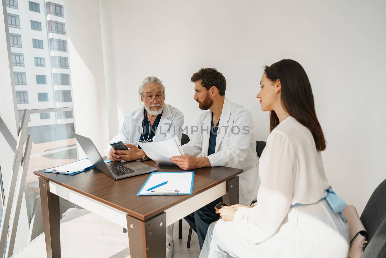 Two doctors in white uniform consult female patient at meeting in private medicine clinic by Yaroslav_astakhov