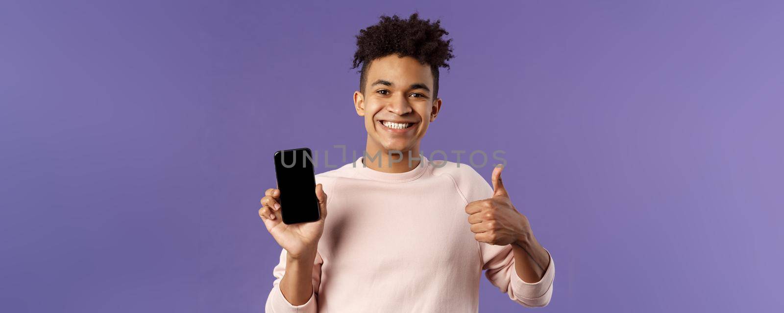 Close-up portrait of cheerful, satisfied young male customer recommend buying subscribtion to game or app, learning leanguage via application mobile phone, show thumb-up in approval.