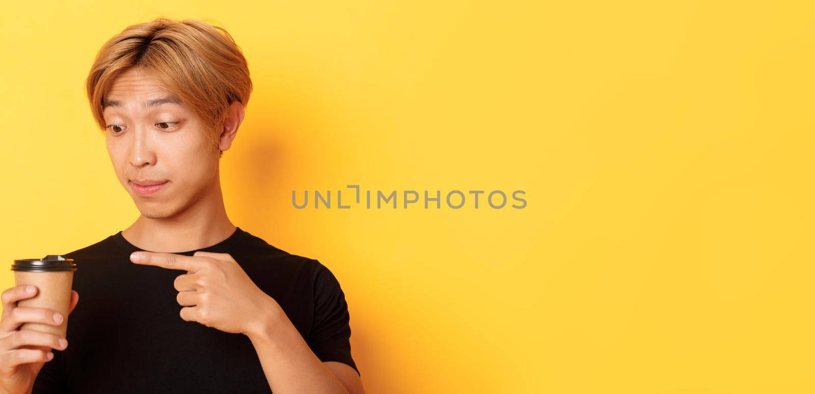 Close-up of impressed handsome asian guy pointing finger at delicious coffee, standing amazed over yellow background by Benzoix