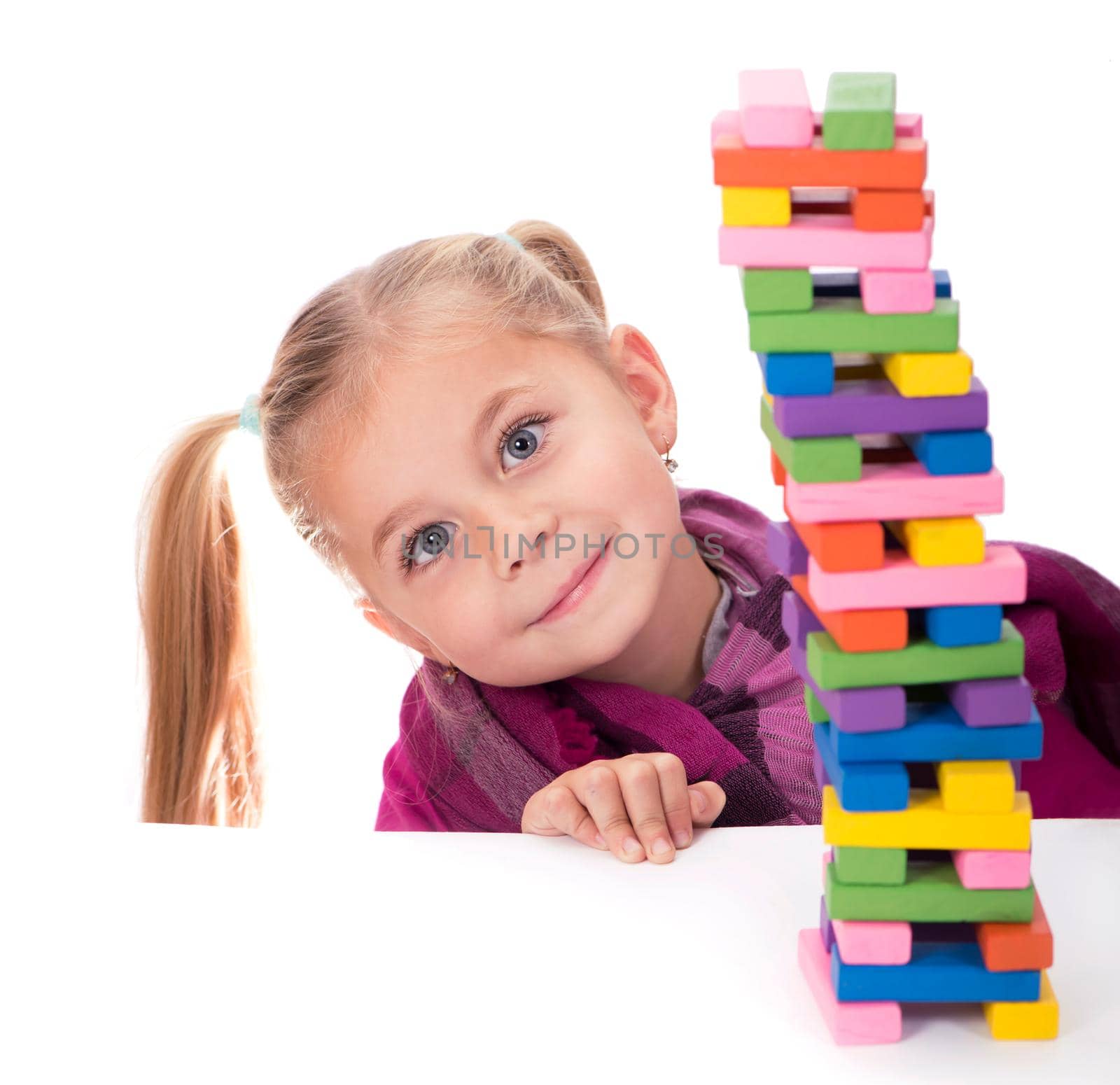 Children's hobbies, creativity, a little girl in a blue dress playing with the wood game jenga on white background by aprilphoto