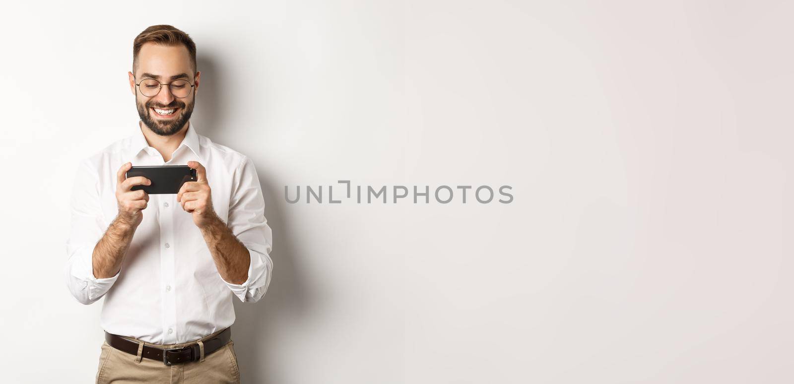 Happy businessman watching video on mobile phone, standing over white background.