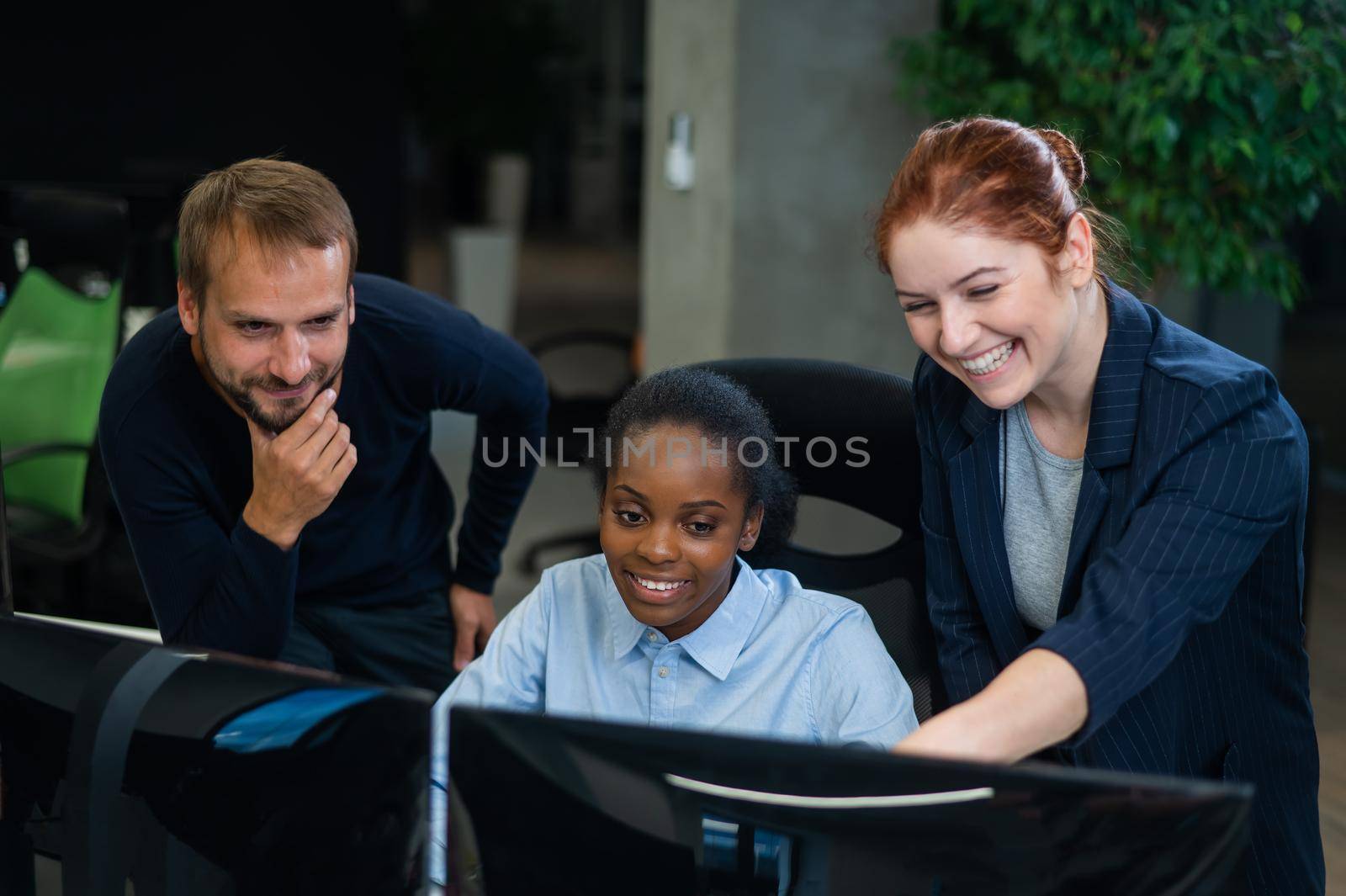 Colleagues look at the monitor and decide working moments. African young woman, caucasian man and red-haired caucasian woman communicate in the office. by mrwed54