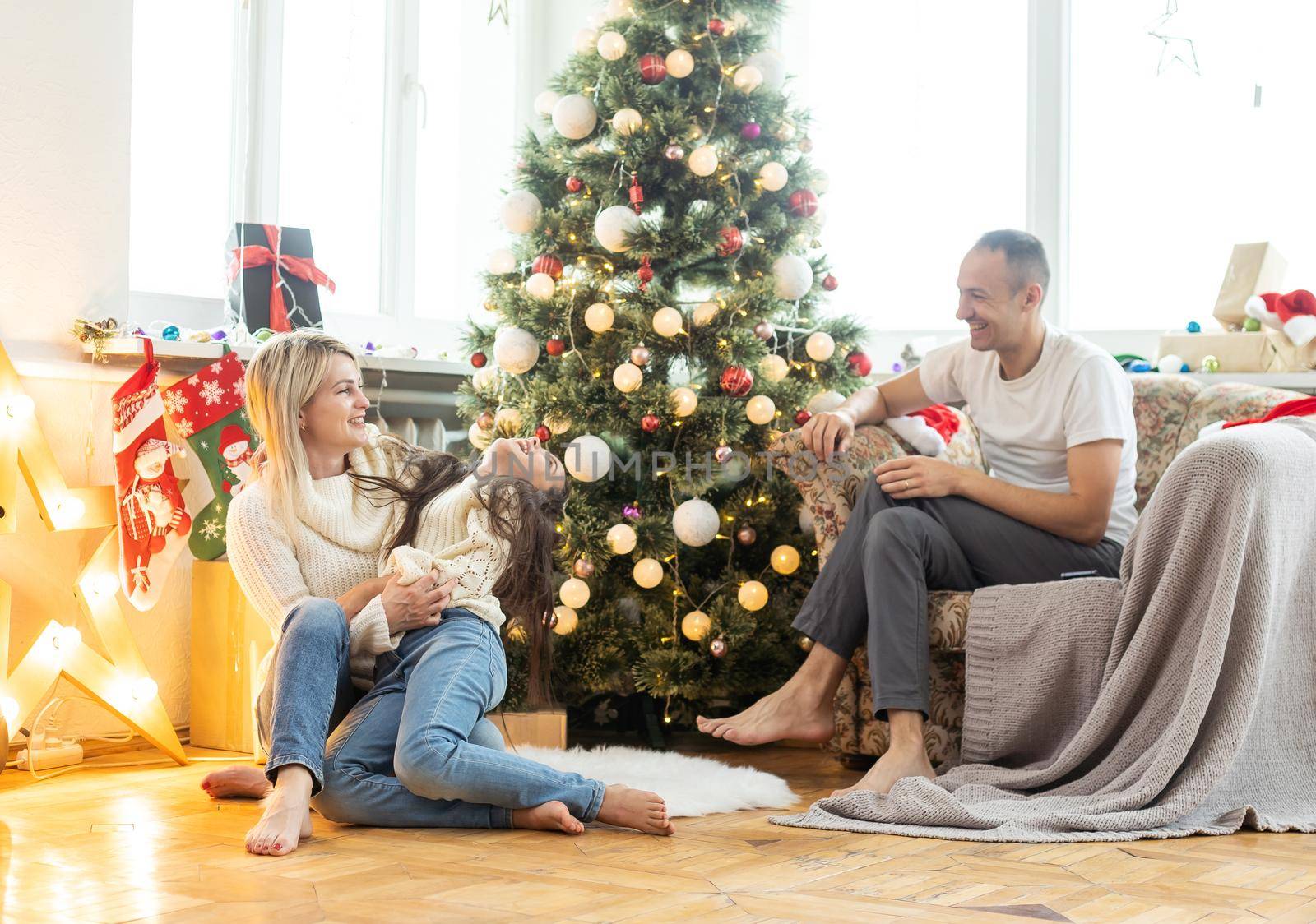 Beautiful young family enjoying their holiday time together, decorating Christmas tree, arranging the christmas lights and having fun
