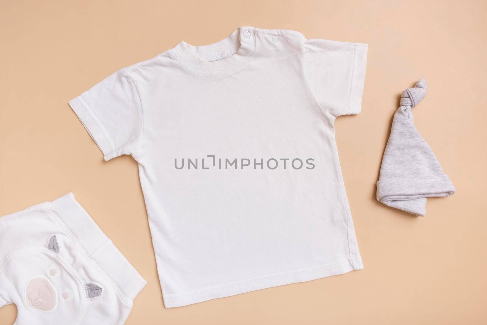 White baby t-shirt top view. Mockup for logo, text or design on beige background. Flat lay child clothers by ssvimaliss