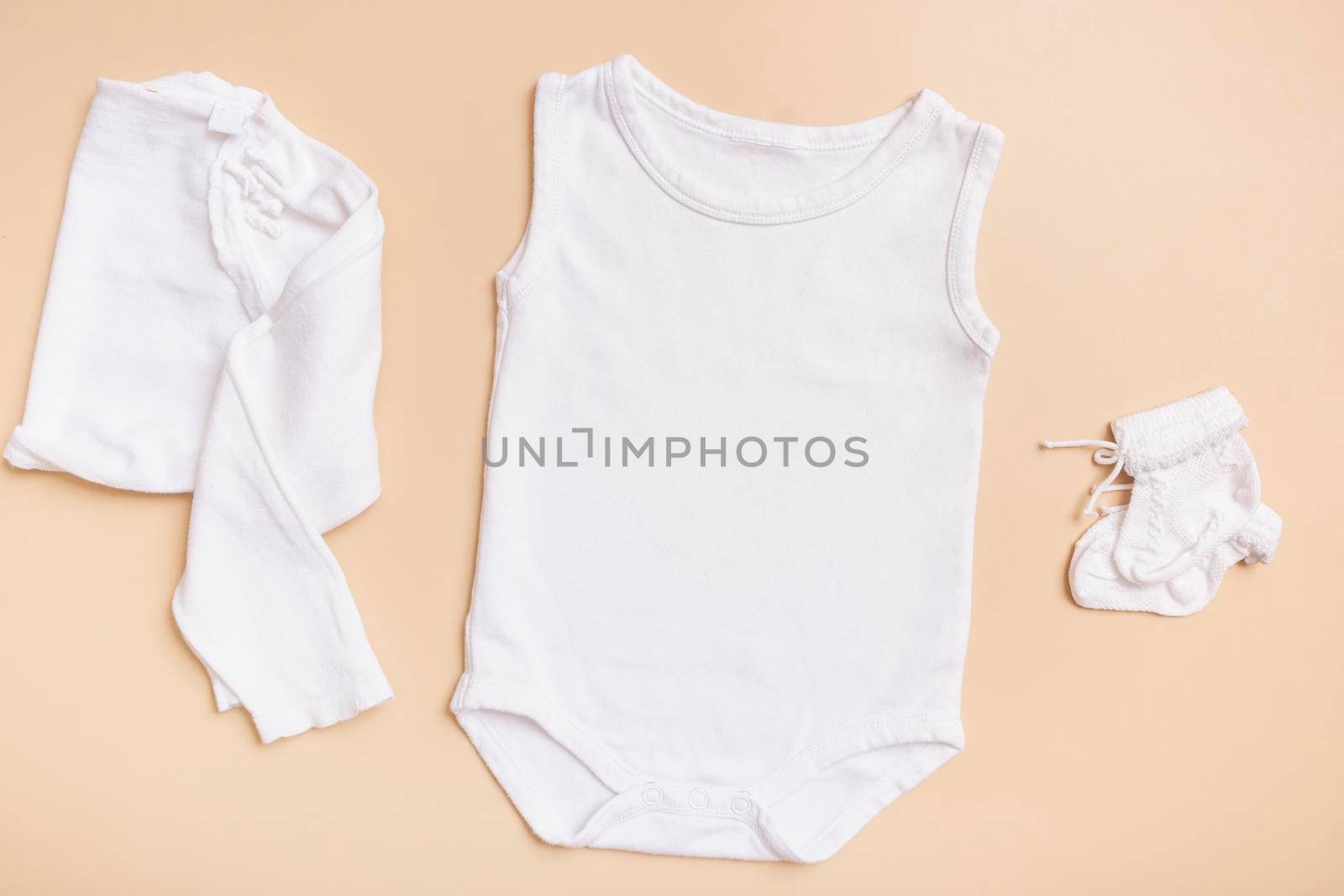 White baby bodysuit mockup for logo, text or design on beige background with clothes top view by ssvimaliss