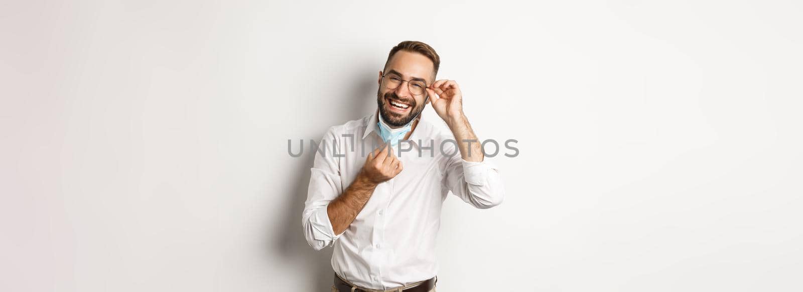 Covid-19, social distancing and quarantine concept. Happy businessman take off face mask and smiling, standing over white background by Benzoix