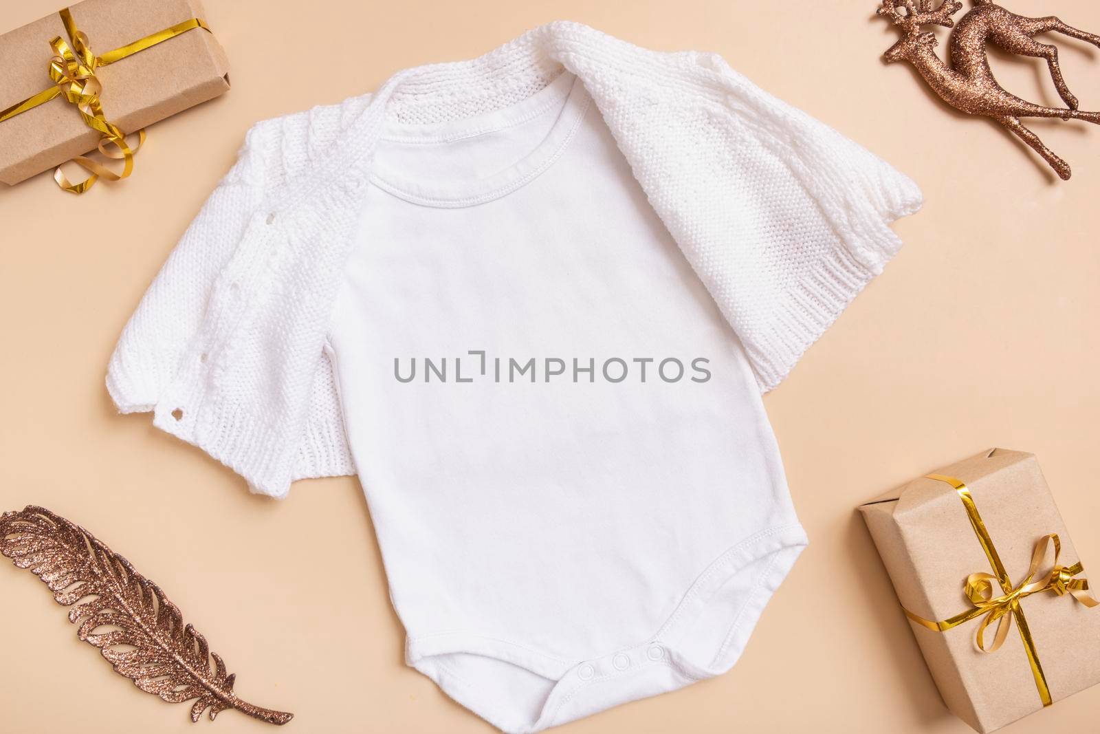 White baby bodysuit mockup for logo, text or design on beige background with winter decotations top view by ssvimaliss