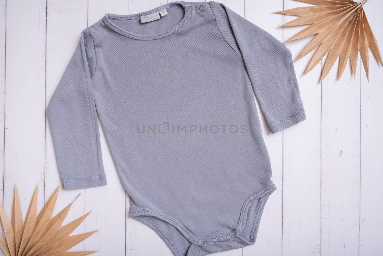 Grey baby bodysuit top view. Mock up for logo, text or design on wooden background. Flat lay with palm leaves.