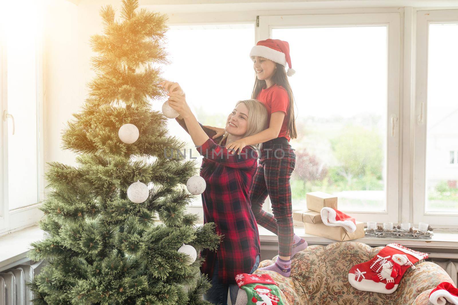 family, winter holidays and people concept - happy mother and little daughter decorating christmas tree at home