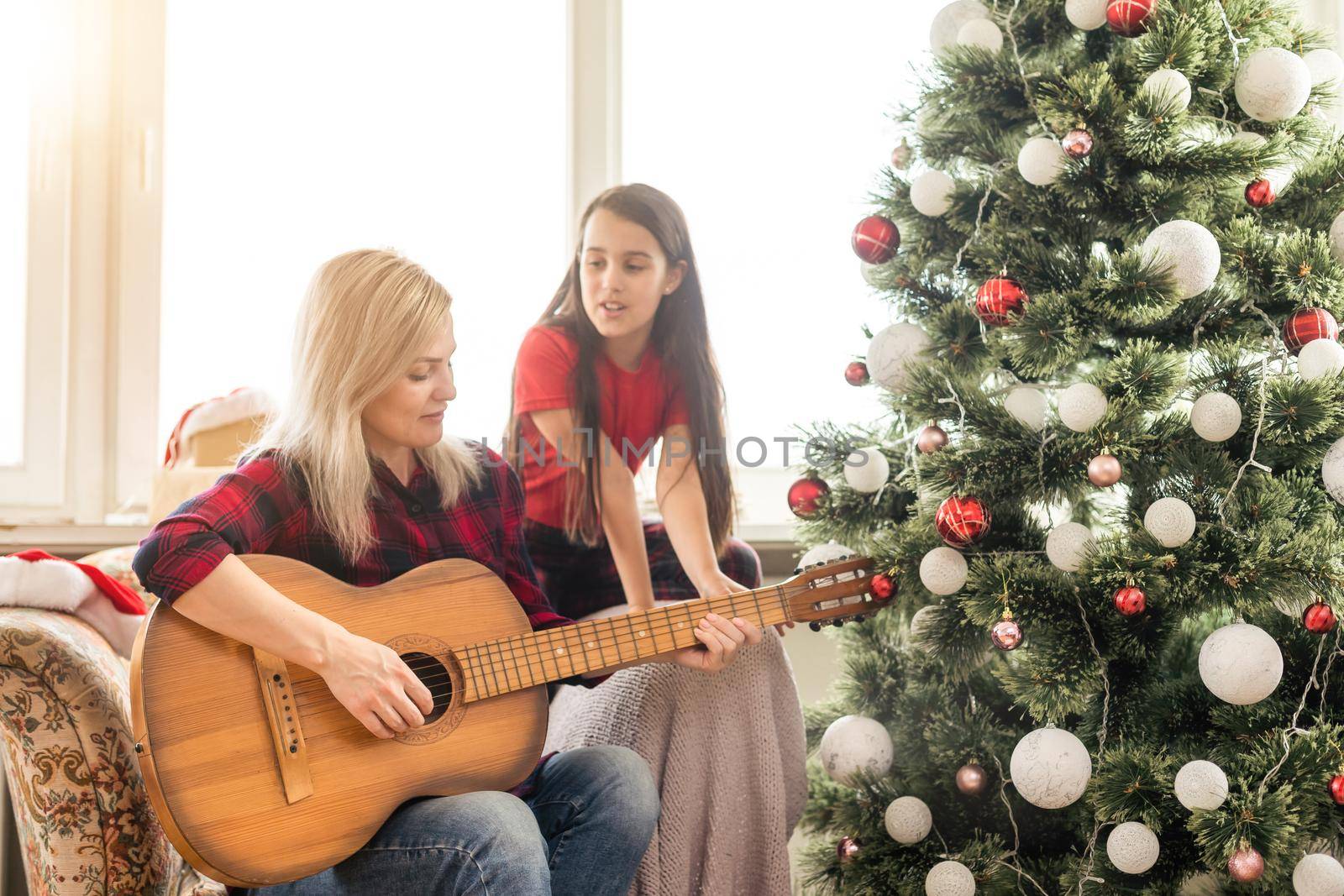 family, winter holidays and people concept - happy mother and little daughter decorating christmas tree at home