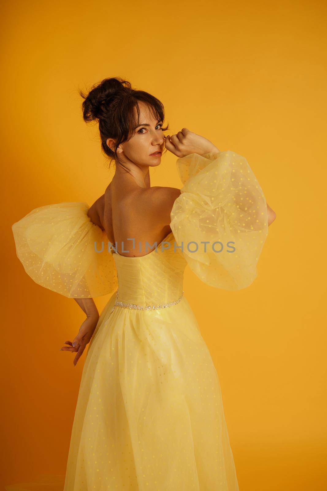 Portrait of a beautiful middle-aged woman in a yellow dress, her hair pulled up against a yellow background by Matiunina