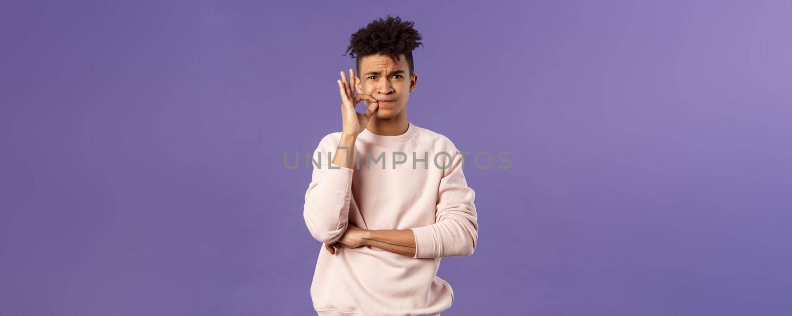 Portrait of serious-looking hispanic 25s young man promise to keep his mouth shut, secret is safe, zip his lips, lock it on key, hiding something cause he swear, standing purple background.