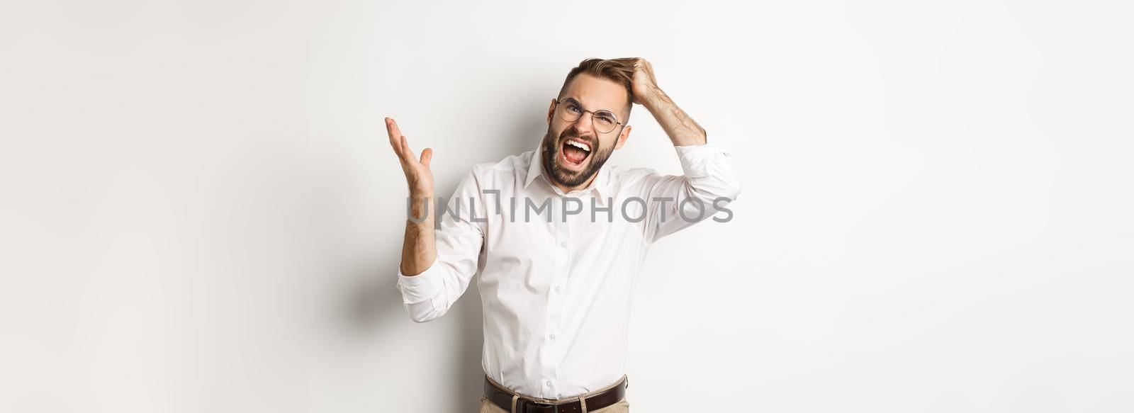 Confused and annoyed man scratching head, arguing and complaining, standing over white background.