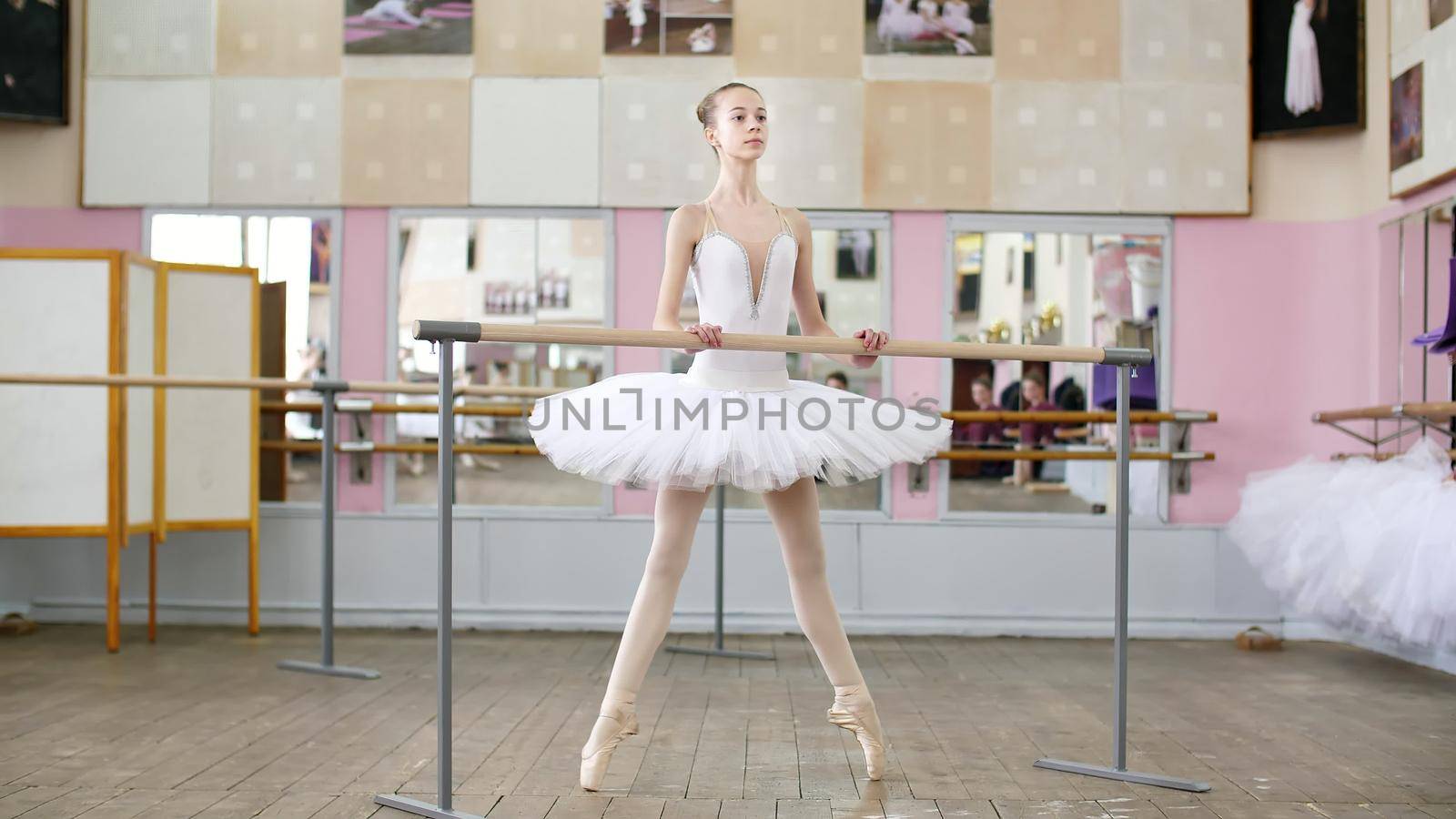 in the ballet hall, girl in white pack is engaged at the ballet, rehearse Roleve, goes up on toes, in pointe shoes , Young ballerina standing at railing in ballet hall. High quality photo
