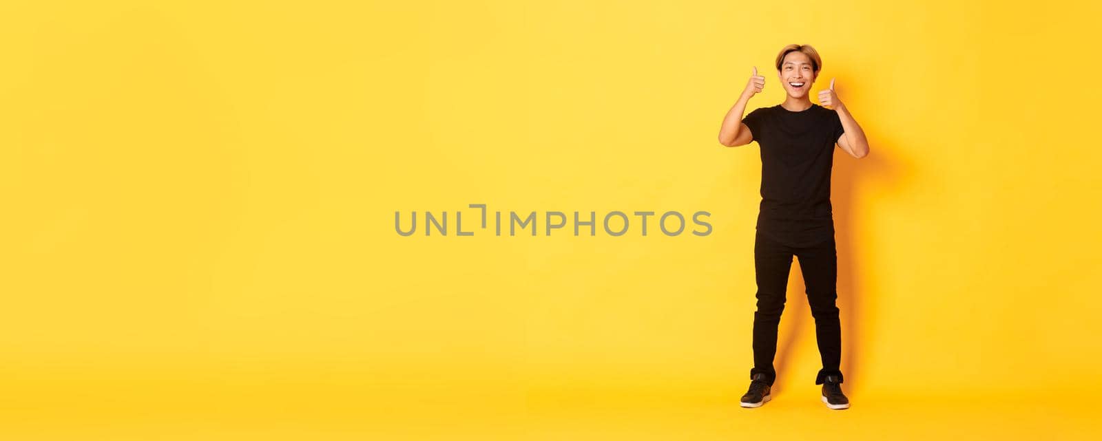 Full-length of satisfied handsome asian guy smiling, showing thumbs-up in approval, yellow background by Benzoix