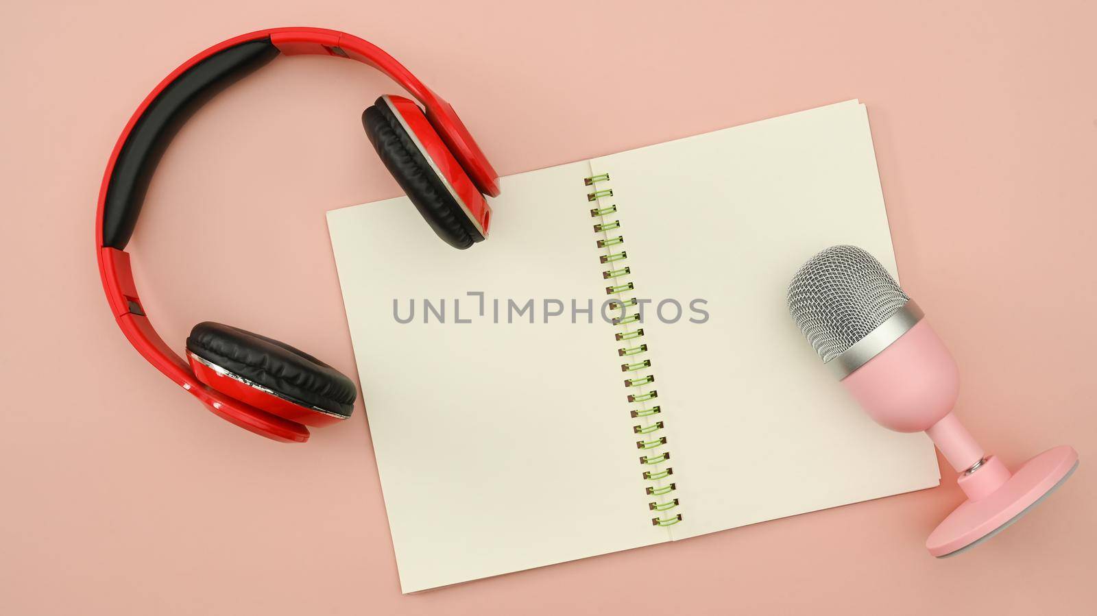 Red wireless headphone and microphone and empty notepad on pink background. Technology and audio equipment concept.