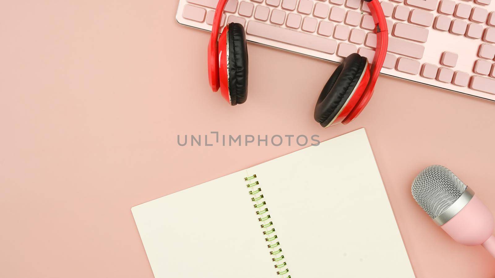 Red wireless headphones, microphone and notepad on pink background. Technology and audio equipment concept.