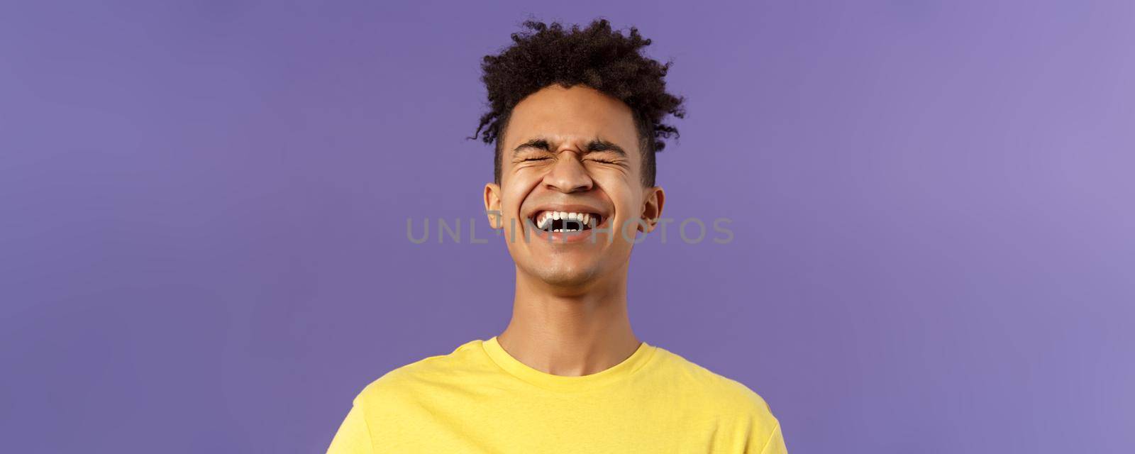 Close-up portrait of happy carefree young guy laughing loud, chuckling over hilarious joke, bending backwards and close eyes while giggle over funny movie, purple background.