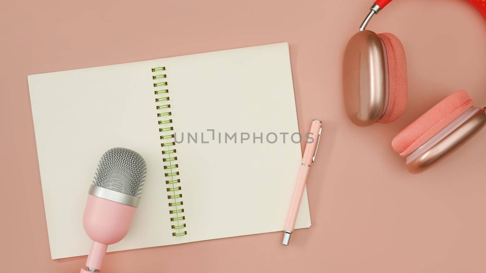 Blank notebook, microphone for podcasts and wireless headphones on pink background.