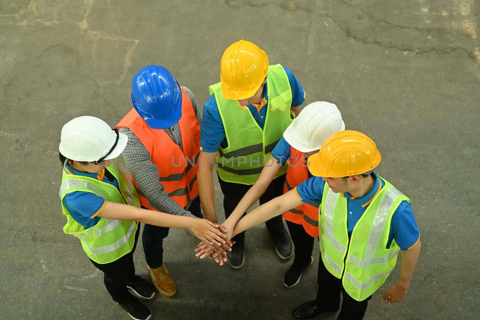 Overhead view of warehouse workers in hardhats and reflective vests stacking hands together. Logistics, storehouse occupation.