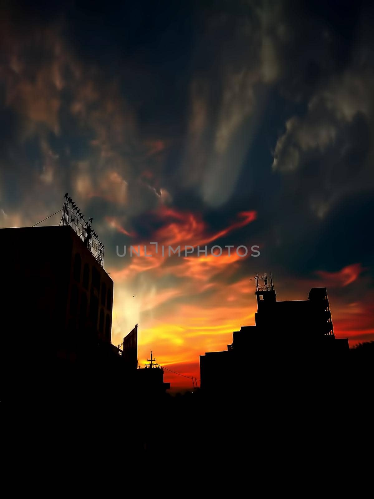 Sunset Dusk time shot of clouds and sun setting in background along with some silhouette of buildings also. by mirzamlk