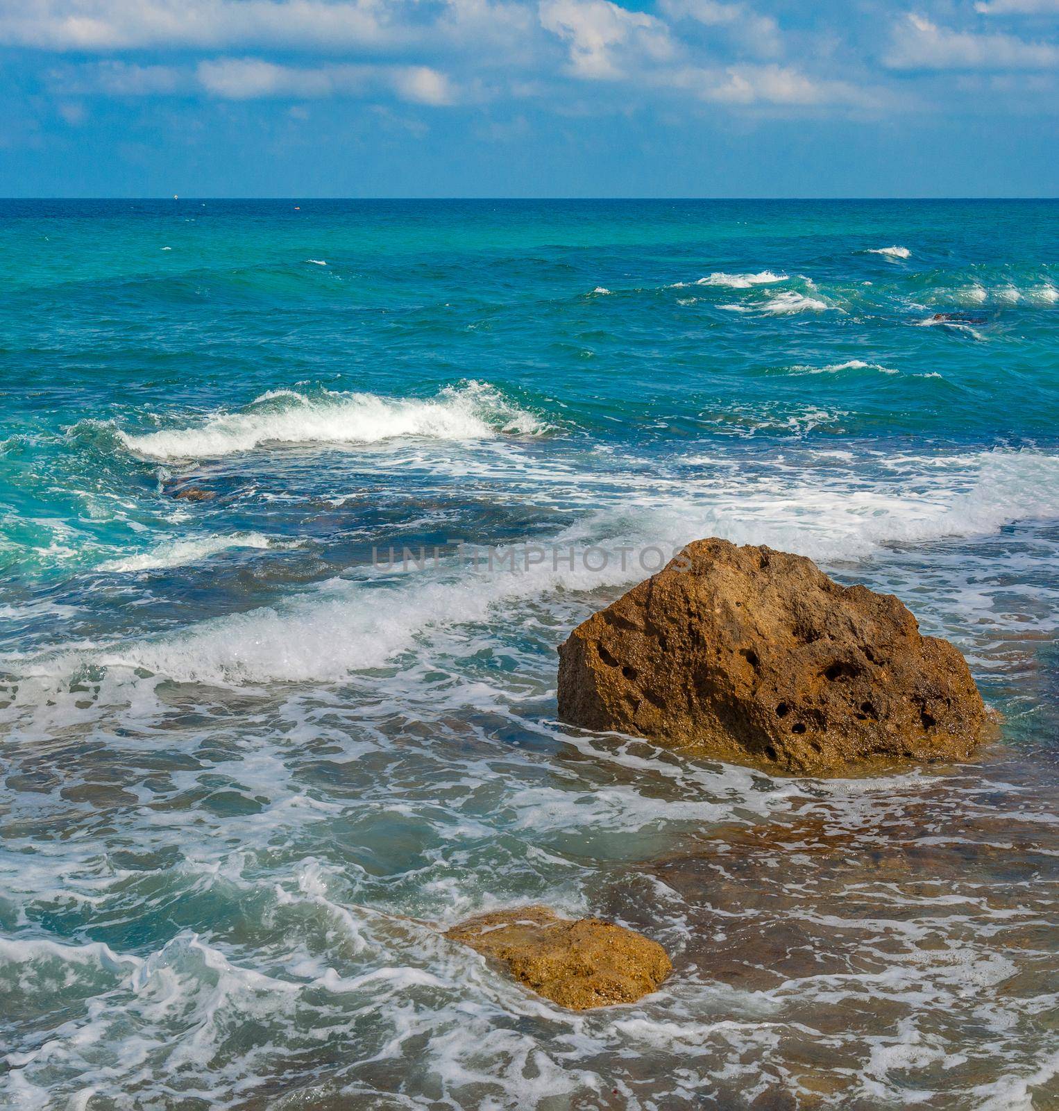 High tide in the Mediterranean Sea, warm, foamy waves run up the coastal rocks and gradually cover them with sea water