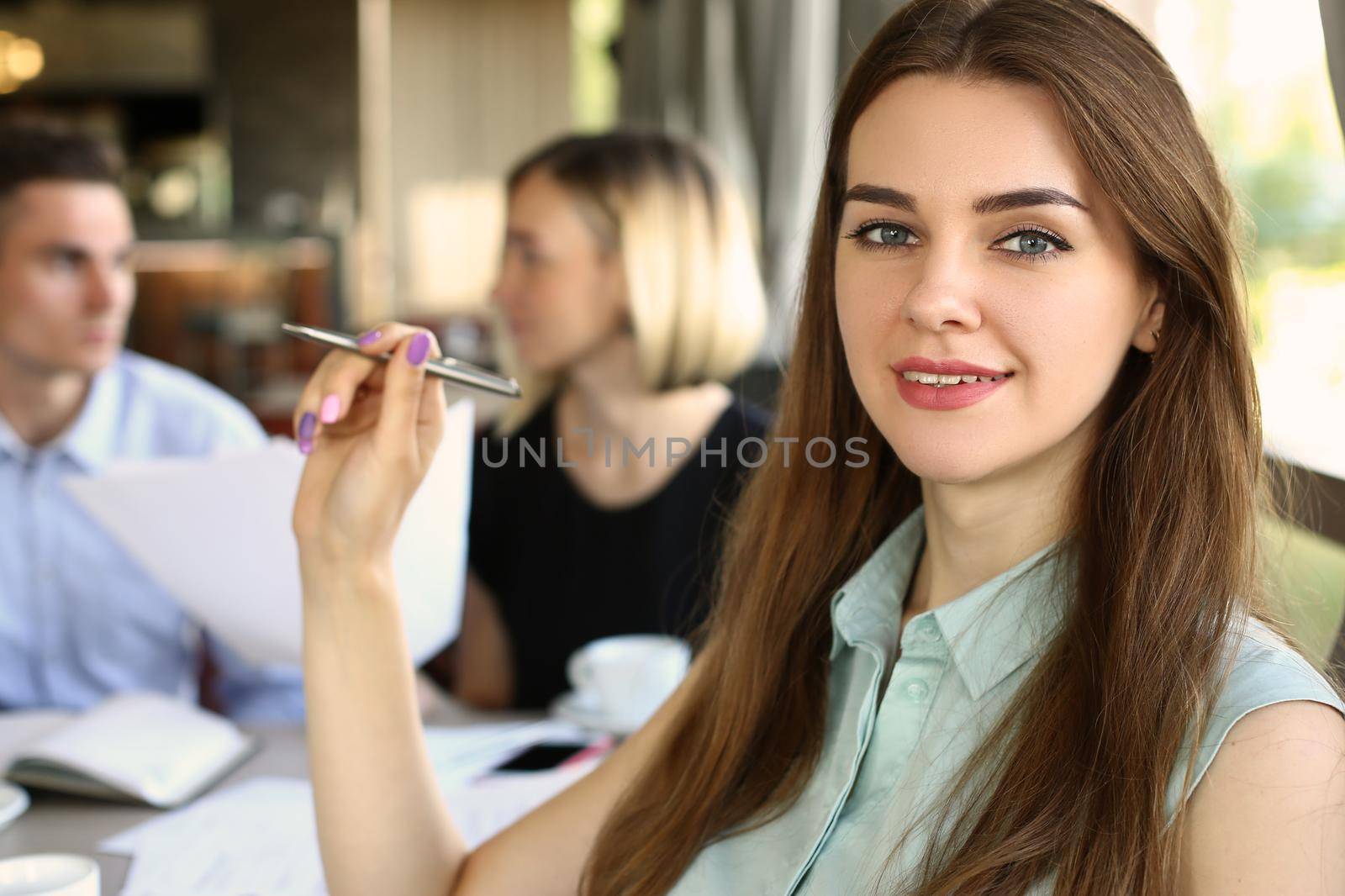 Portrait of a beautiful business woman sitting in cafe with colleagues discussing business project in background. Business meeting and discussion of business development