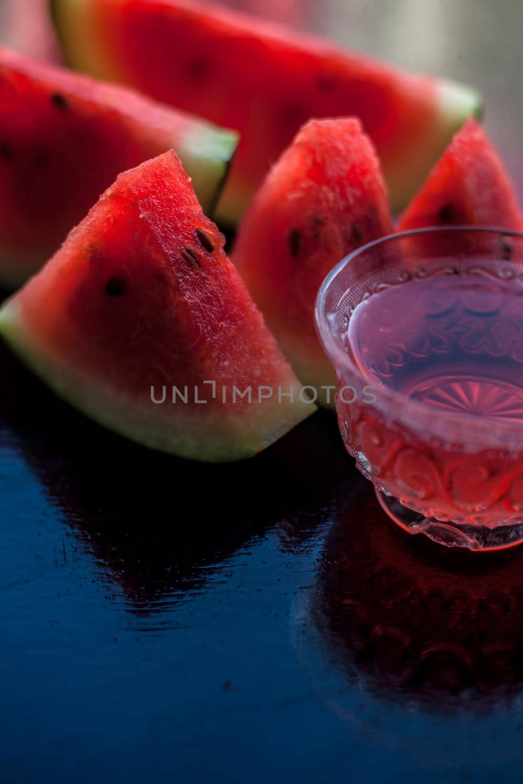 Vertical shot of fruit ice tea of watermelon seeds in a transparent glass cup on wooden surface along with triangular pieces of watermelon.