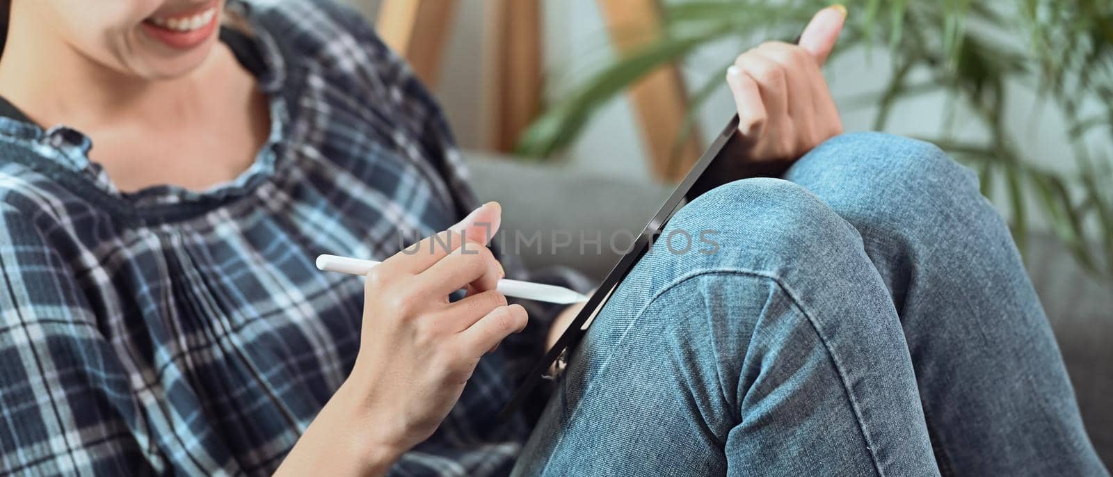 Cropped shot smiling woman working online with digital tablet on sofa.