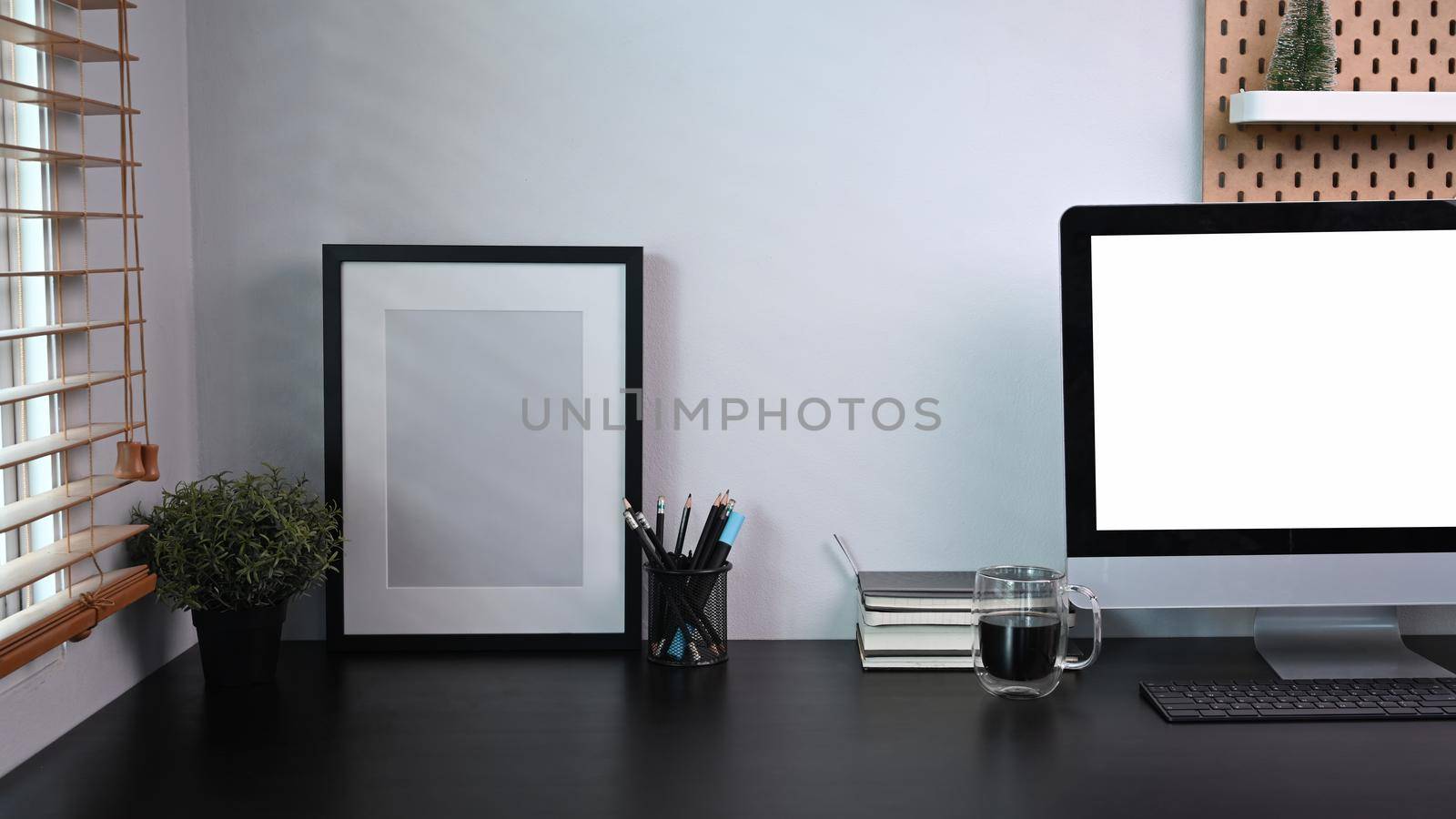 Picture frame, computer with blank screen and houseplant on black table.