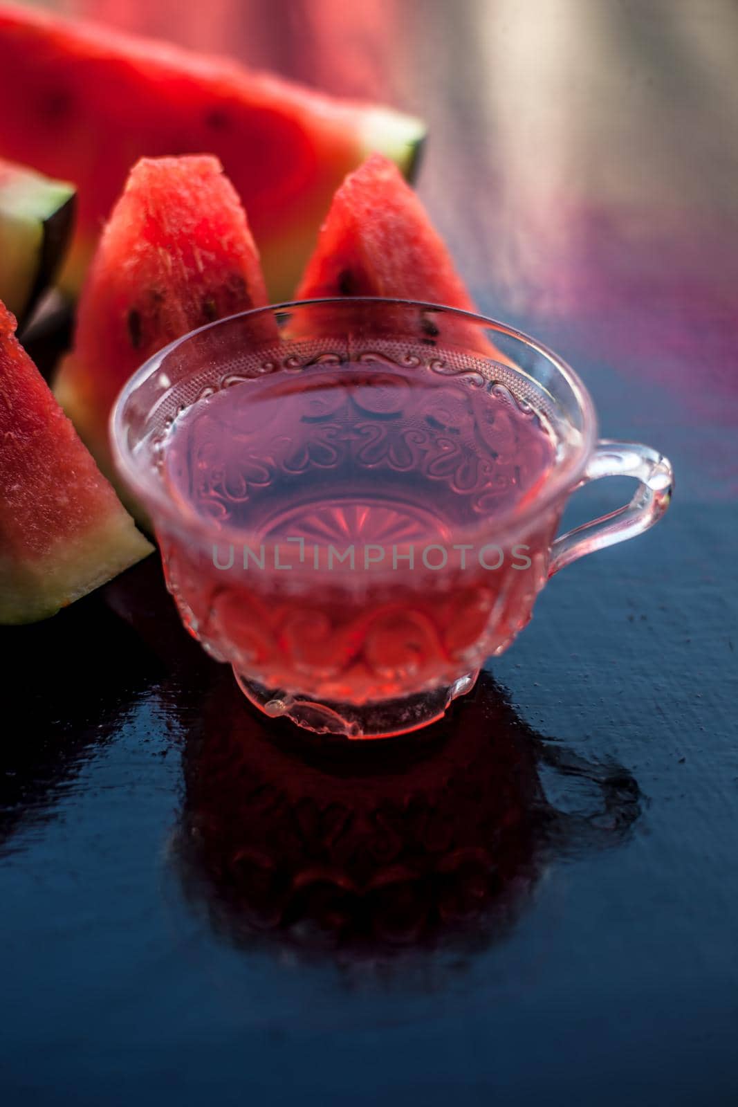 Mouth-watering watermelon tea in a transparent glass cup on wooden surface with watermelon pieces in triangle shape. by mirzamlk