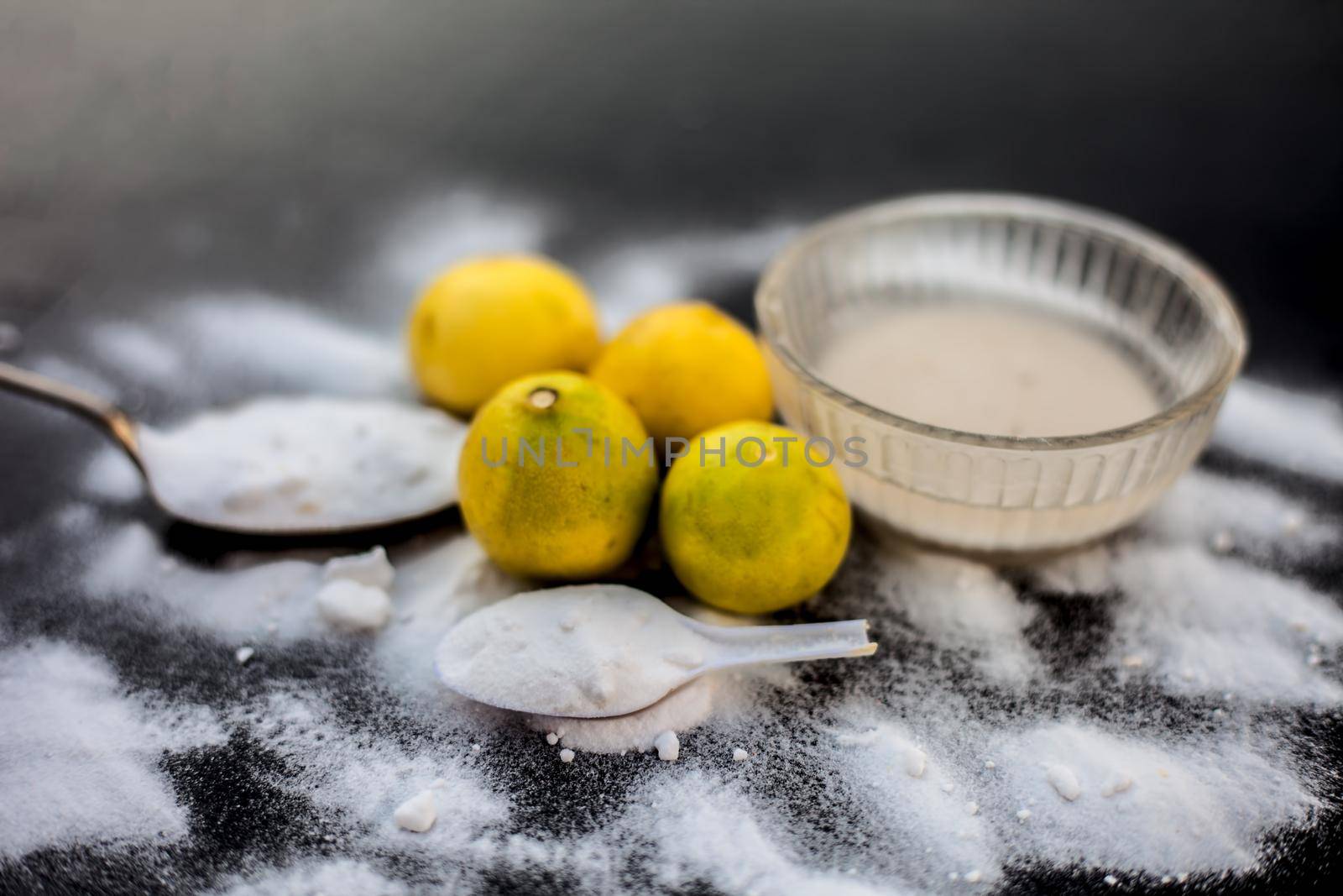 Baking soda face mask in a glass bowl on wooden surface along with some baking soda sprinkled on the surface and lemons also on surface. Used to blemishes skin instantly. by mirzamlk