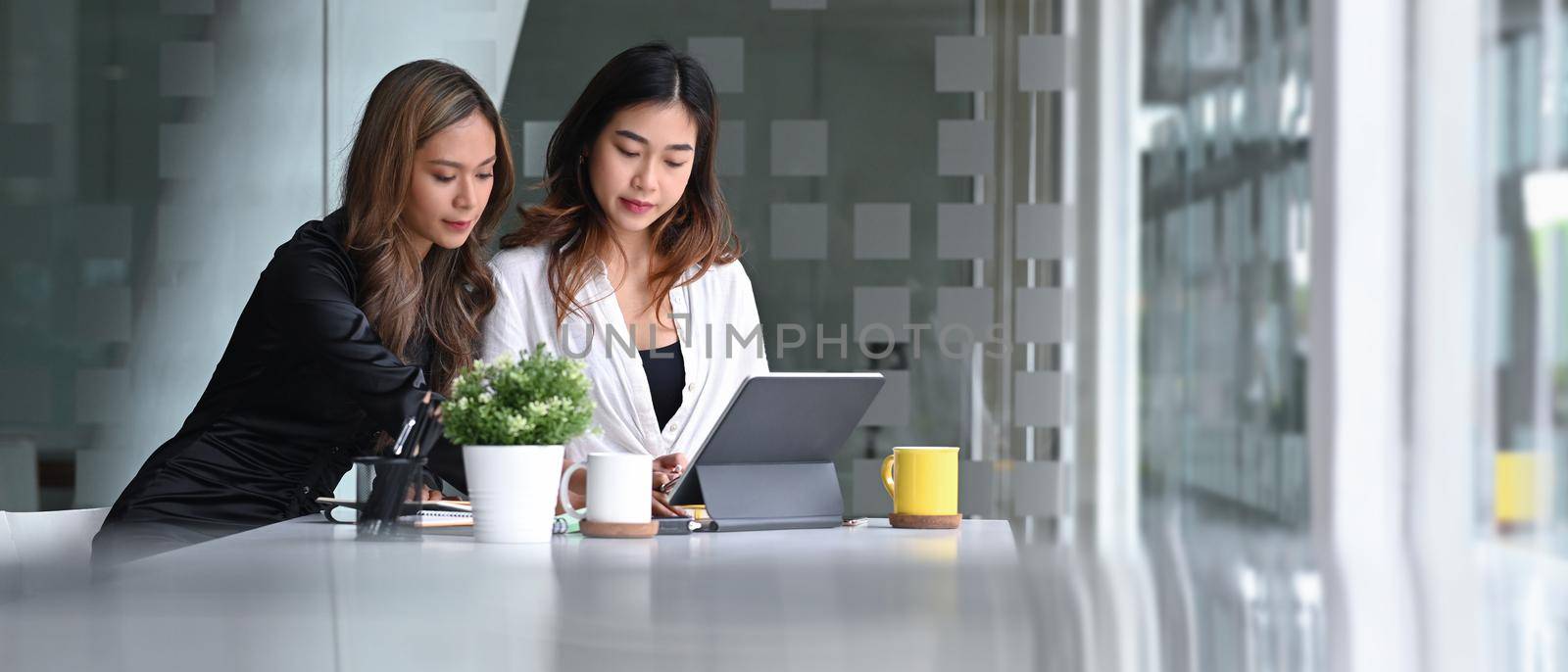 Two female colleagues discussing about a new project together at the office. by prathanchorruangsak