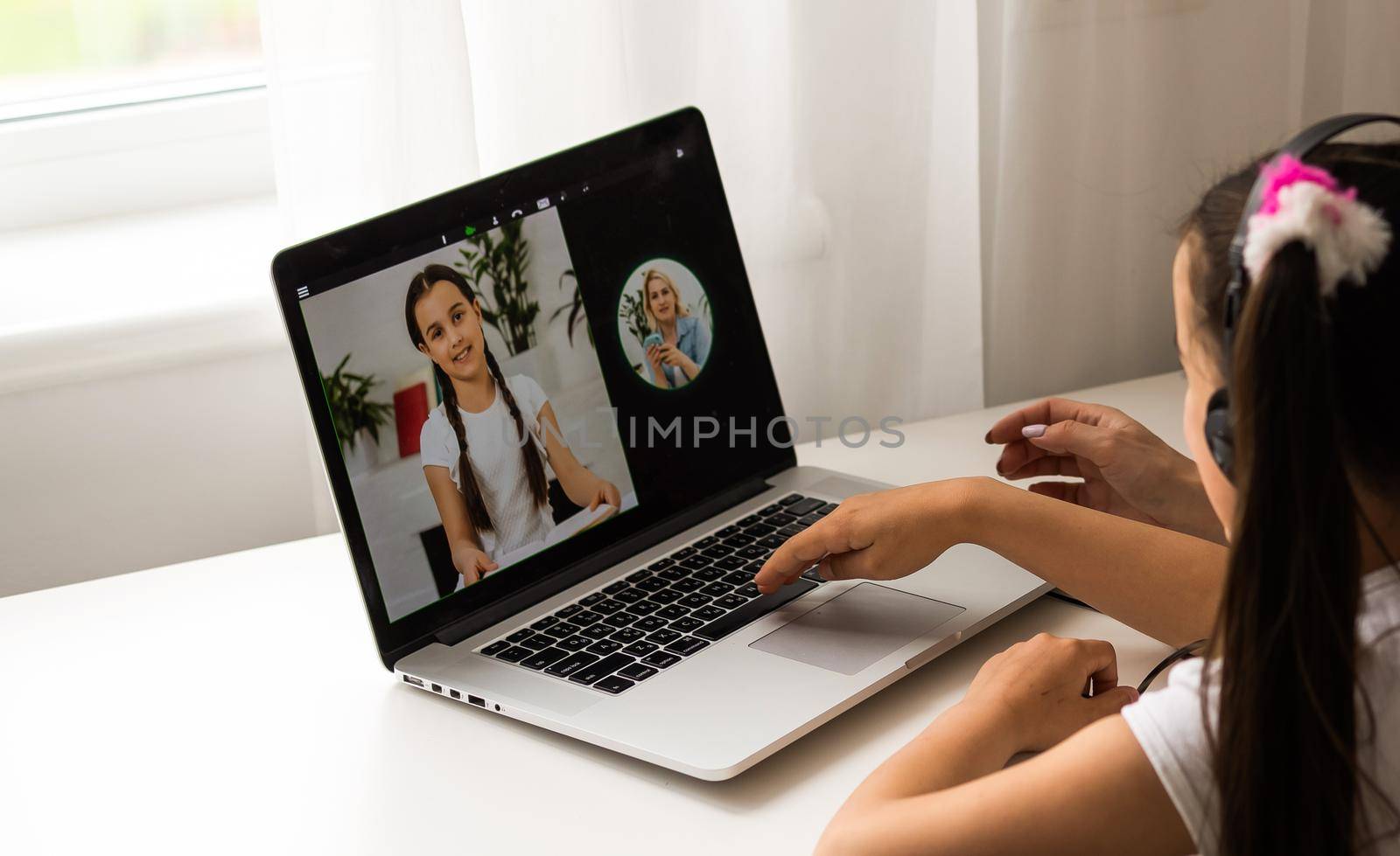 Homeschool little young girl learning online class from school teacher by digital remote internet meeting due to coronavirus pandemic. Kid looking computer and writing note with help from mother.